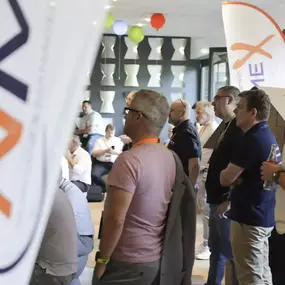 Teilnehmer bei Networking-Event auf Messe, Firmenbanner und Ballons im Raum